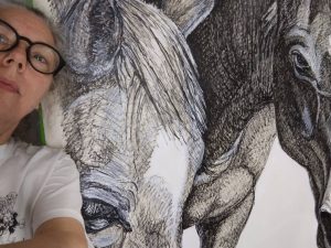 The artist stands in front of a 4-foot square drawing of horses in progress.
